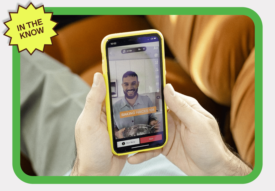 A man smiles while holding a phone with a sticker that reads 